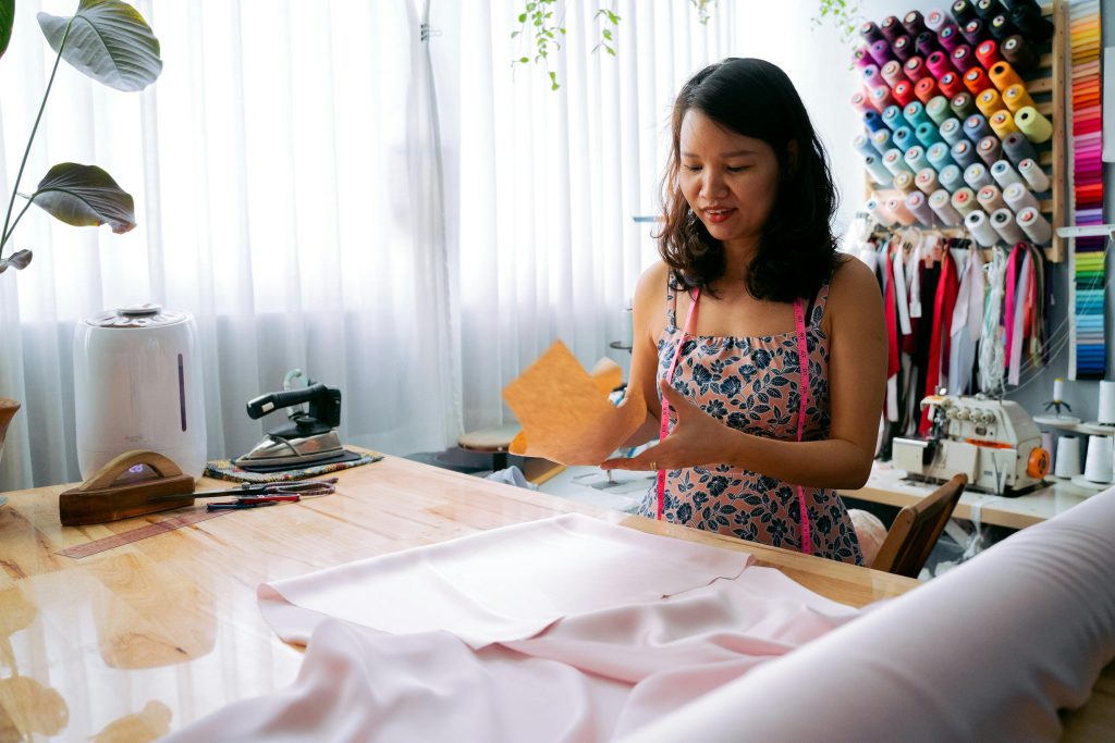 Asian woman working on fabric design in a bright sewing studio filled with colorful materials.