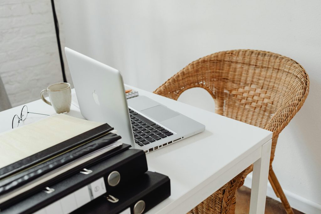 A cozy home office setup featuring a laptop, binders, and wicker chair for productive remote work.