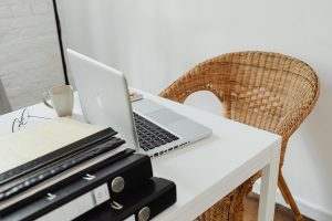 A cozy home office setup featuring a laptop, binders, and wicker chair for productive remote work.